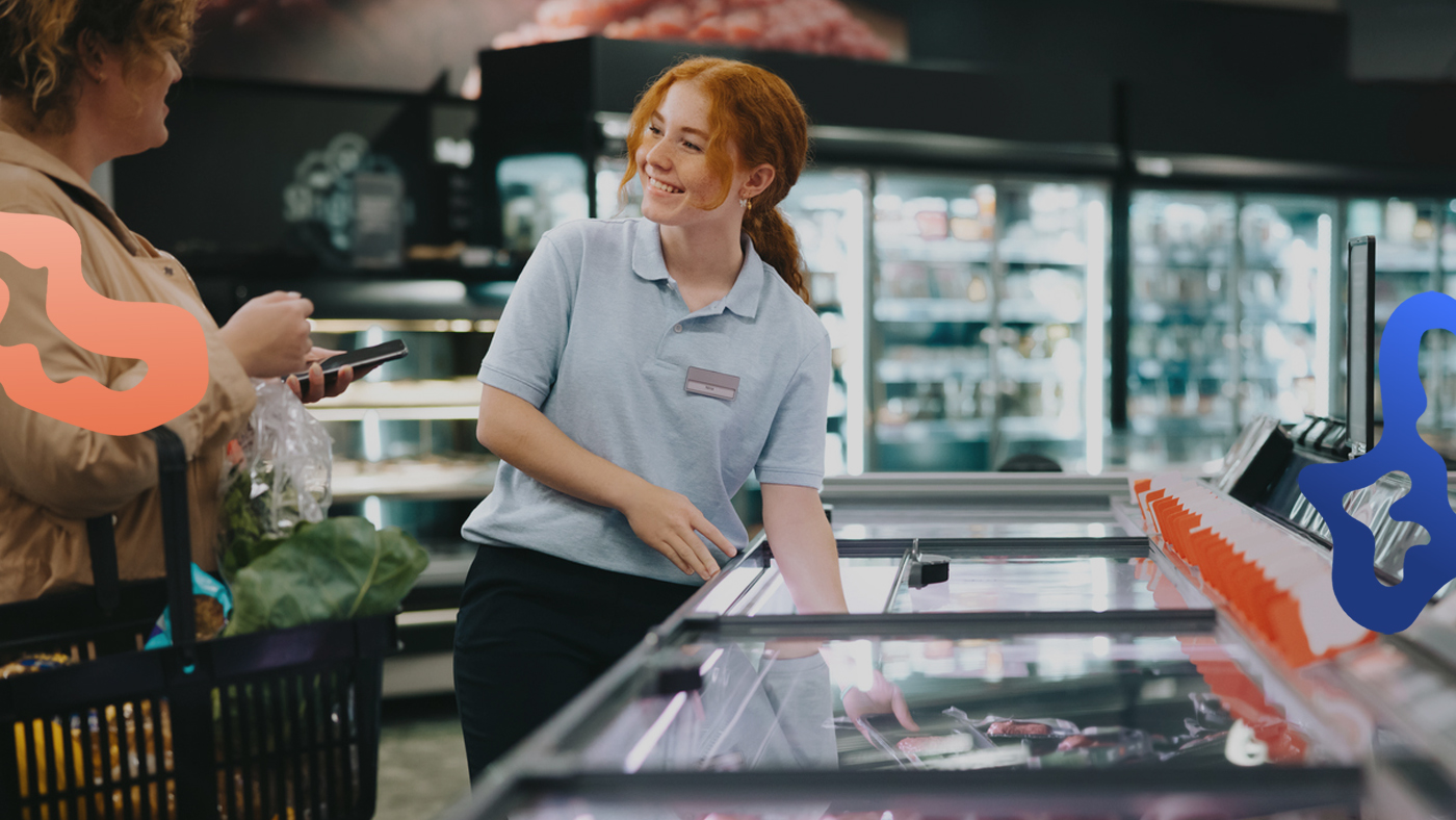 En ung tjej har ett butiksjobb och hjälper en kund i en matbutik.