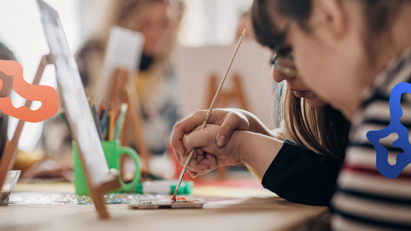 En person som jobbar som resurs i skolan hjälper en elev att måla med pensel.