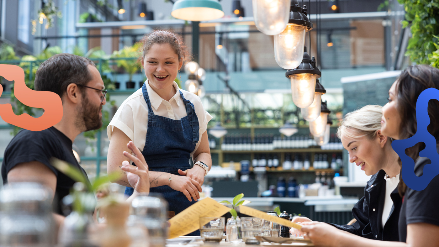 Kvinna med extrajobb på restaurang tar emot en beställning vid ett bord.
