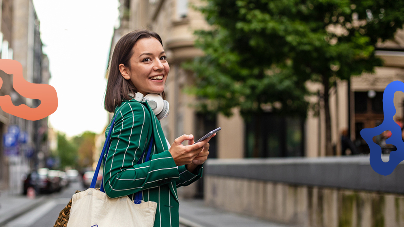 Leende kvinna står i urban miljö och använder smartphone för att lösa sin bemanning med hjälp av Pamoja.